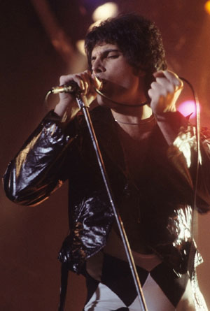 Freddie Mercury signing on stage in a vintage leather jacket.